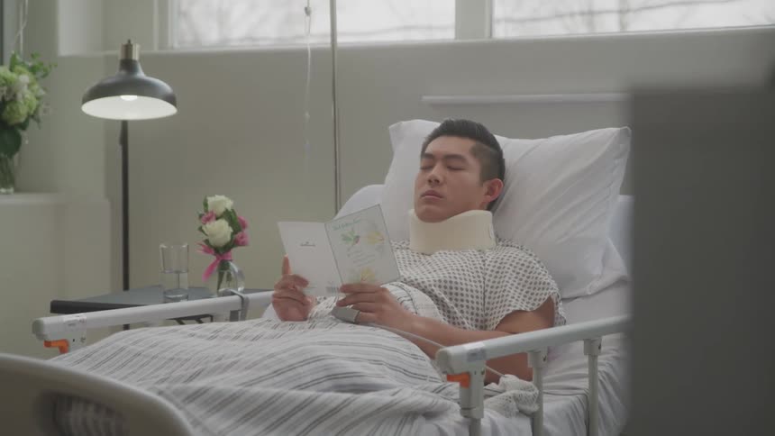 A man lies in a hospital bed reading a get well soon card