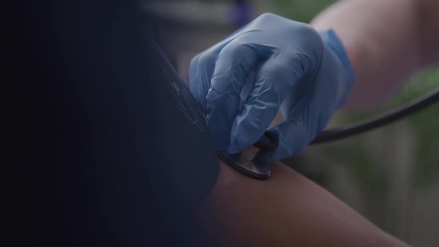 A gloved hand presses a stethoscope to a patients chest during a medical examination