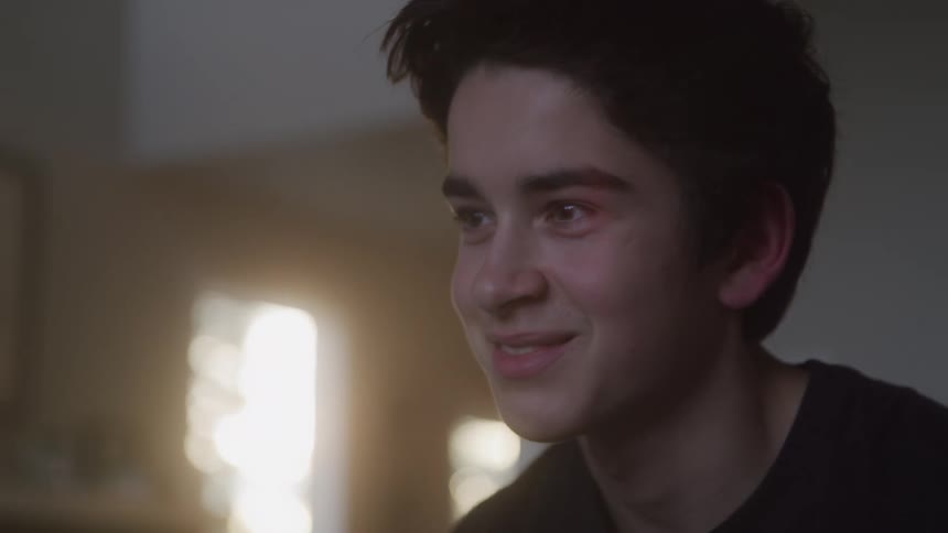 A teenage boy sitting in the living room goes from being sad to smiling and laughing at midday