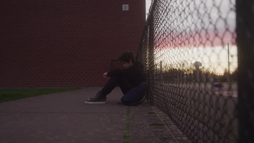 Teenager sitting with his head down on a railing in the late afternoon