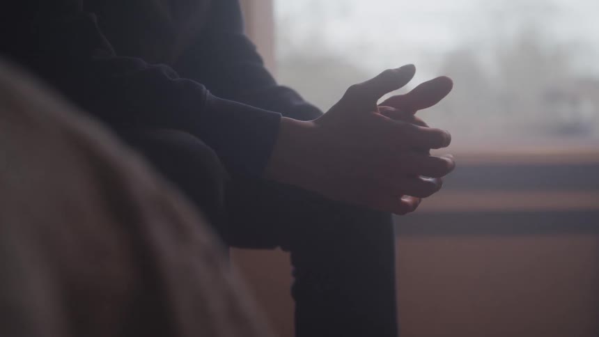 A persons hand is softly extended in a dim backlit setting gender not clearly visible