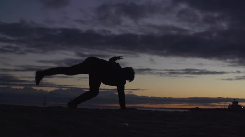Person doing spinning handstand tricks on a beach after sunset