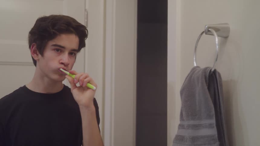 Teen boy brushes teeth in bathroom mirror