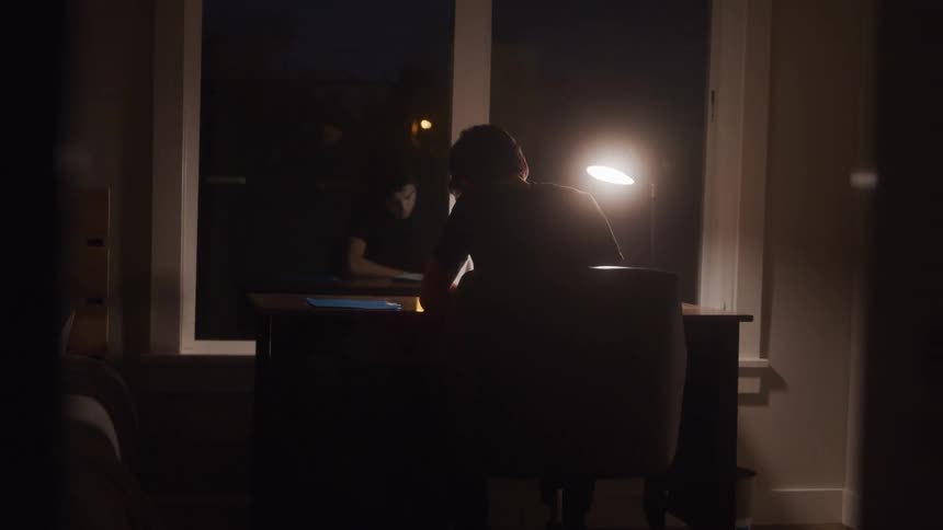 Person studies alone at a desk lit by a lamp during the night