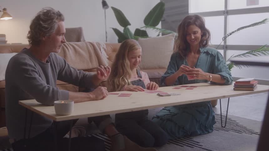 A family plays cards together at a low table in a cozy living room