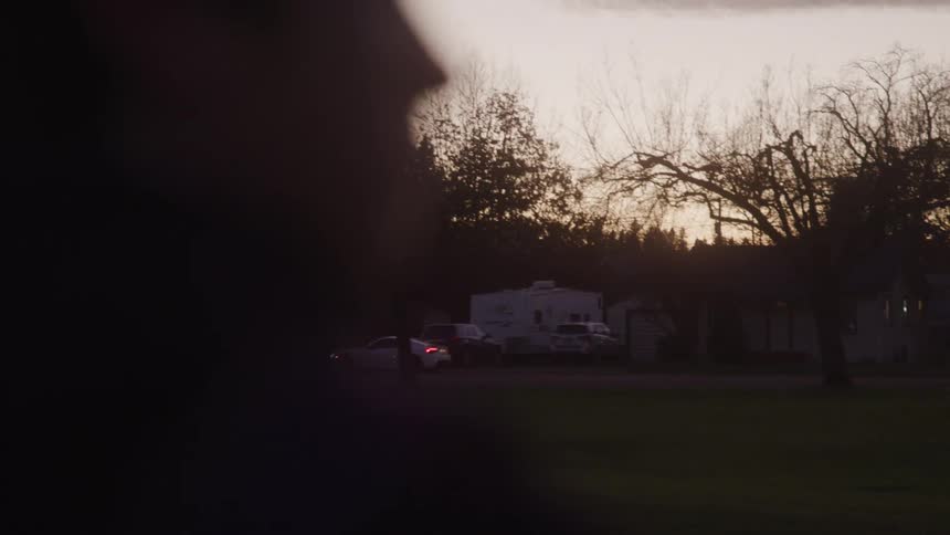 Side silhouette of a persons face in the foreground and in the background of cars passing in the late afternoon through an urban neighborhood