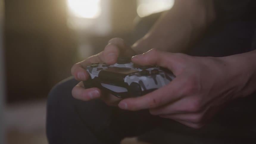 A persons hands are shown gripping and manipulating a black and white video game controller