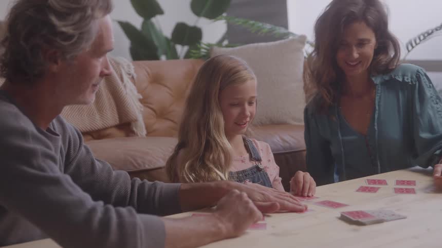 A family sits at a table playing a card game together in a cozy living room