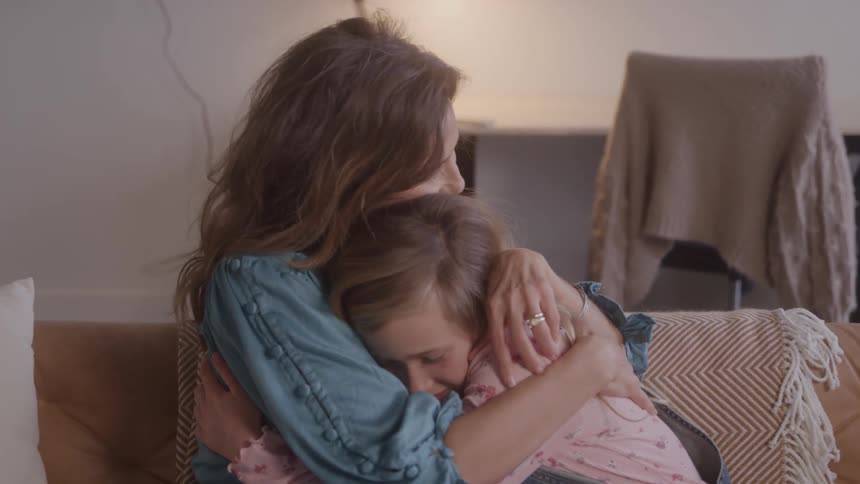 A mother lovingly hugs her daughter on the couch