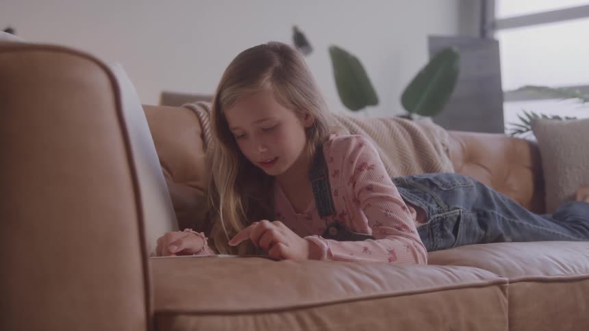 Girl lying on a couch using a tablet in a bright and cozy setting