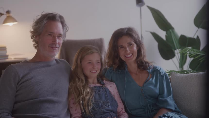 A man woman and young girl sit close together on a couch smiling warmly