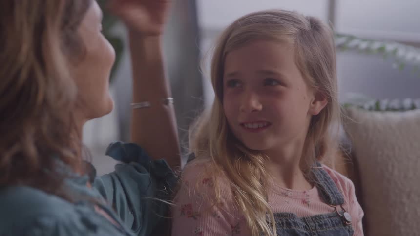 The video shows a tender moment between a mother and her daughter with the mother gently stroking the girls hair the daughter is smiling and leaning in and they share a warm hug at the end