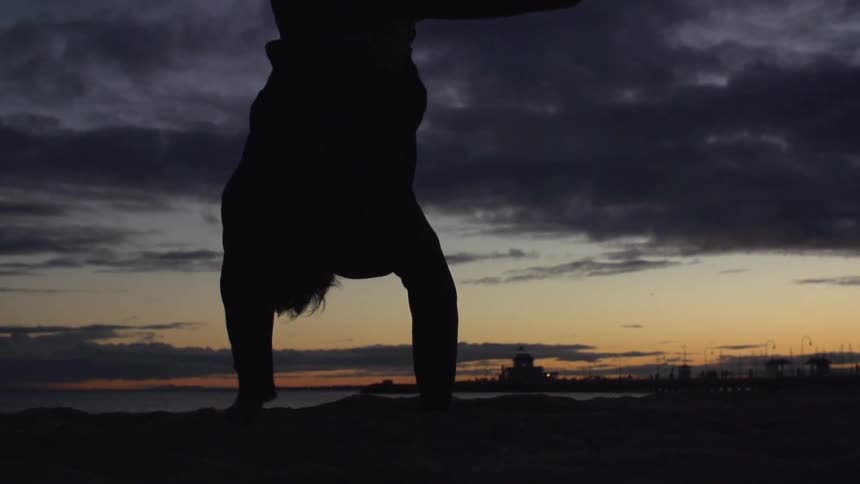 Man doing flips on some sand at sunset