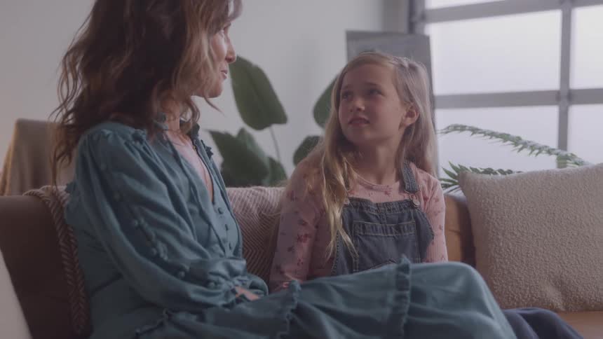 Woman and girl sitting side by side on the couch talking