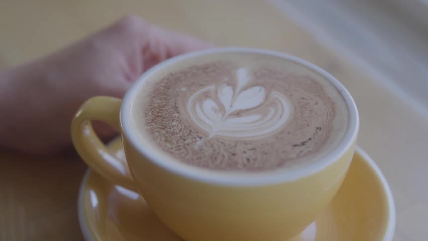 Hand next to a yellow cup with cappuccino coffee