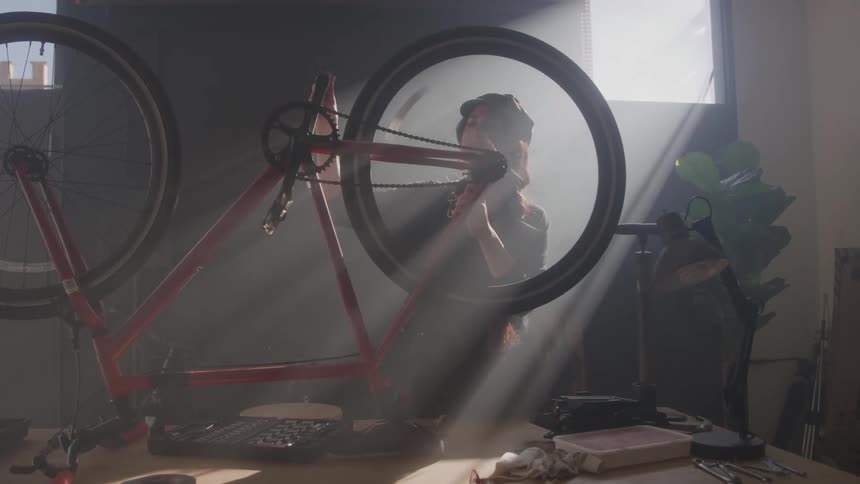 A young woman inside a workshop spins the pedal of a bike watching it as it turns