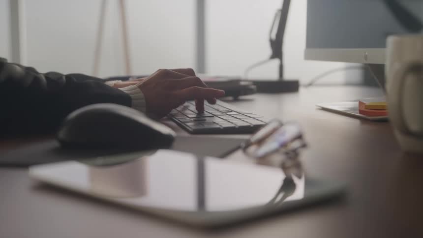 Pair of hands of a person typing on a computer keyboard at a table
