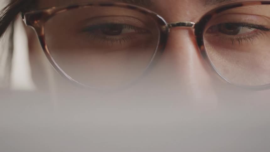 A closeup of a persons eyes shows them looking down while wearing tortoiseshell glasses