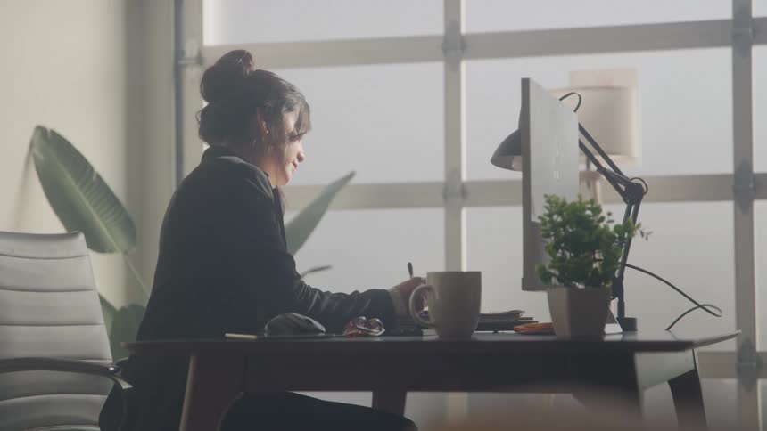 A woman works at a desk with a computer in a sunlit modern office