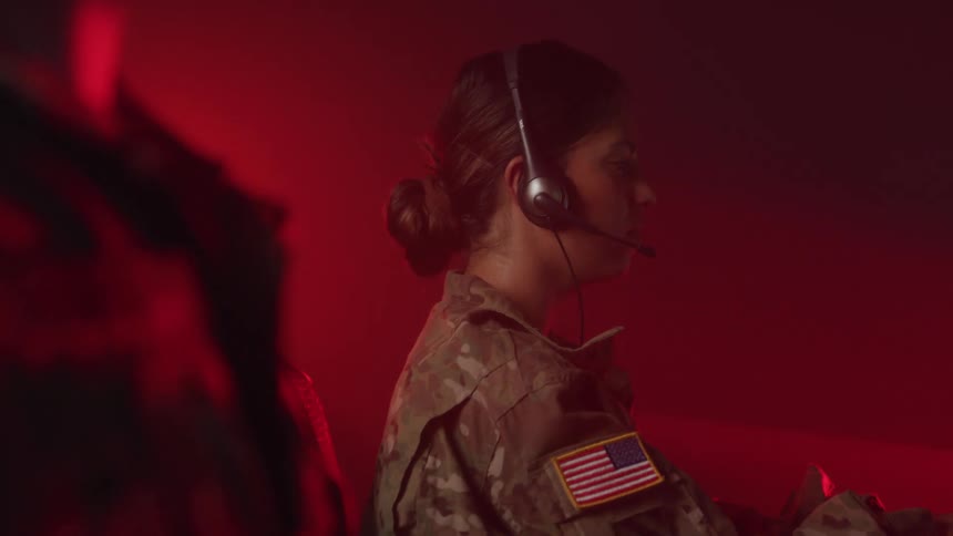 Military woman putting on headset and working in a room in front of a computer with data
