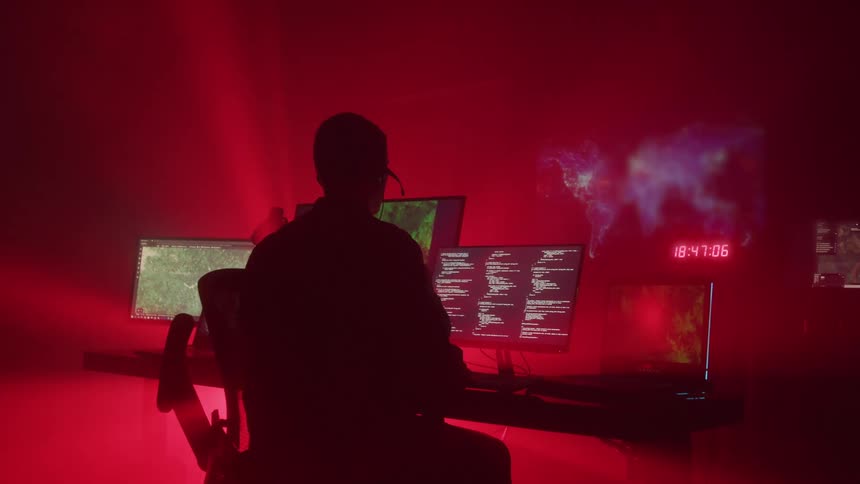 Person working at desk with monitors in a dark control room
