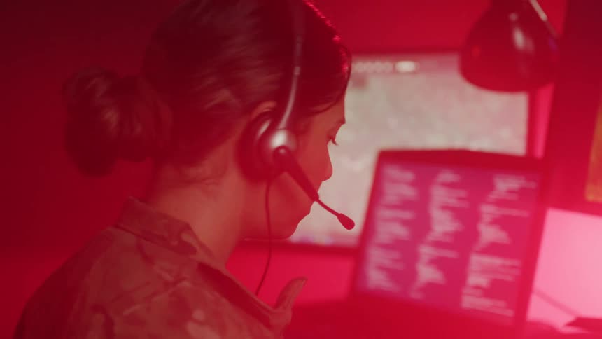 Woman in military uniform communicates via headset in control room