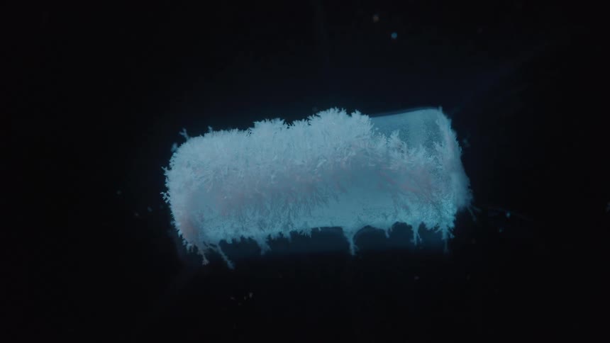 A closeup of a small rectangular patch of liquid on a dark surface the liquid rapidly freezes with white frost spreading from the edges to the center