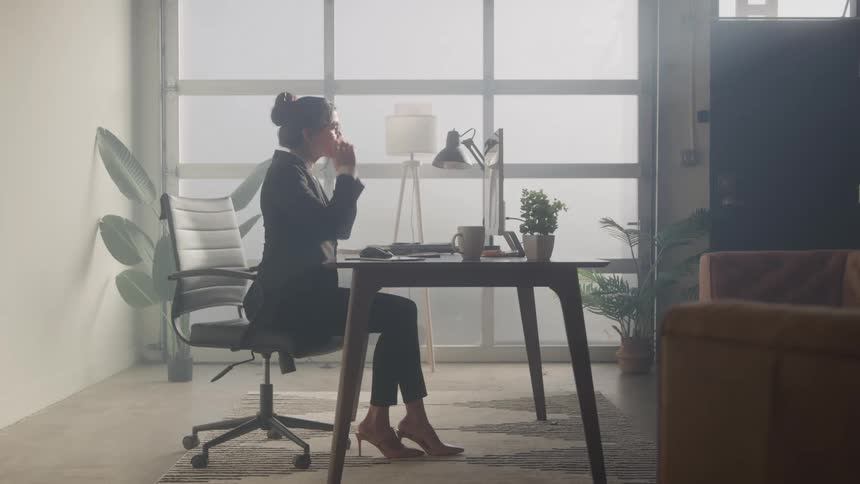 A business woman puts on her glasses while looking at a laptop on her desk