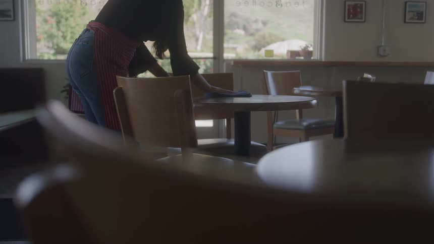 Woman in an apron wiping a table in a restaurant