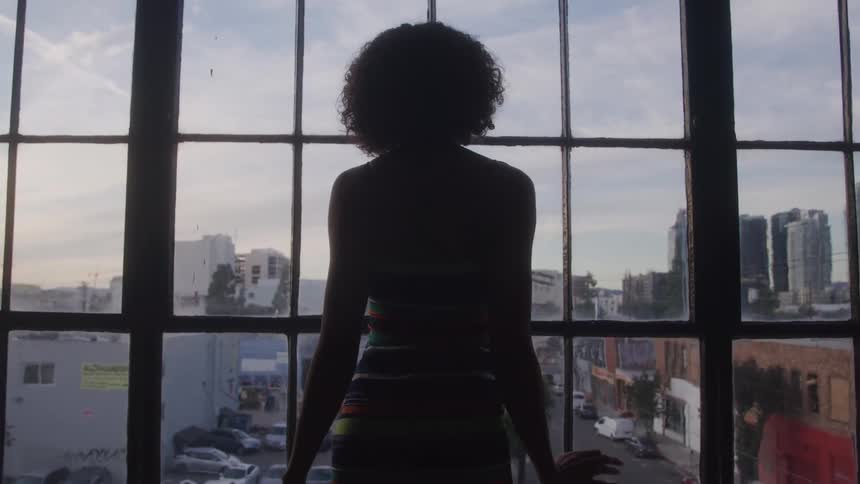 Woman looks at the city through a large window at sunset