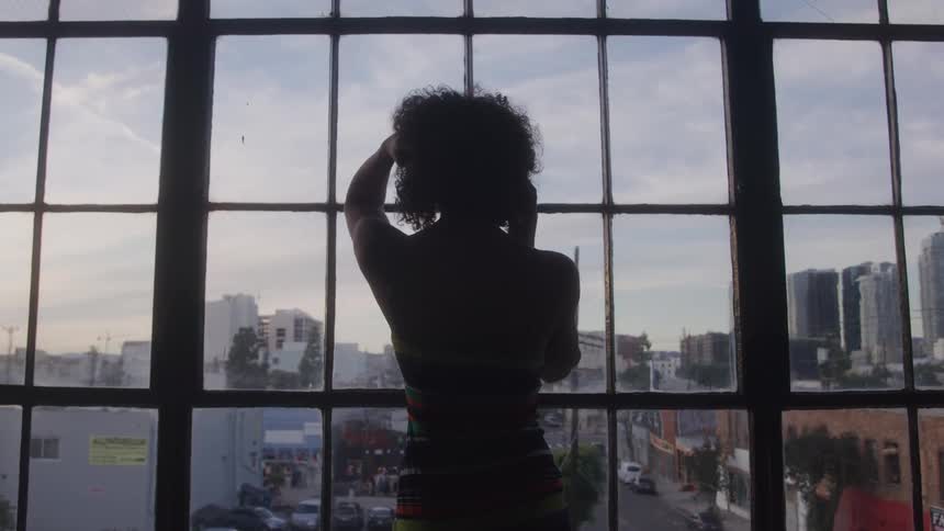 A woman is dancing in front of a window and her back is on camera