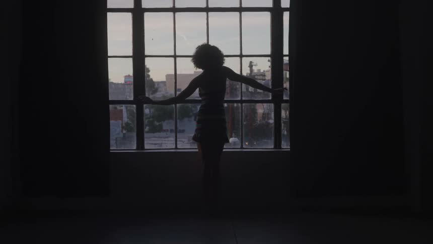 Silhouette of a woman standing in front of a large window at sunset