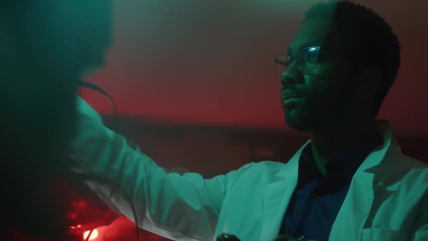 A man in a lab coat checks equipment while writing on a clipboard