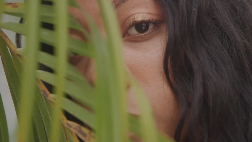 A young woman slowly falls asleep behind palm leaves