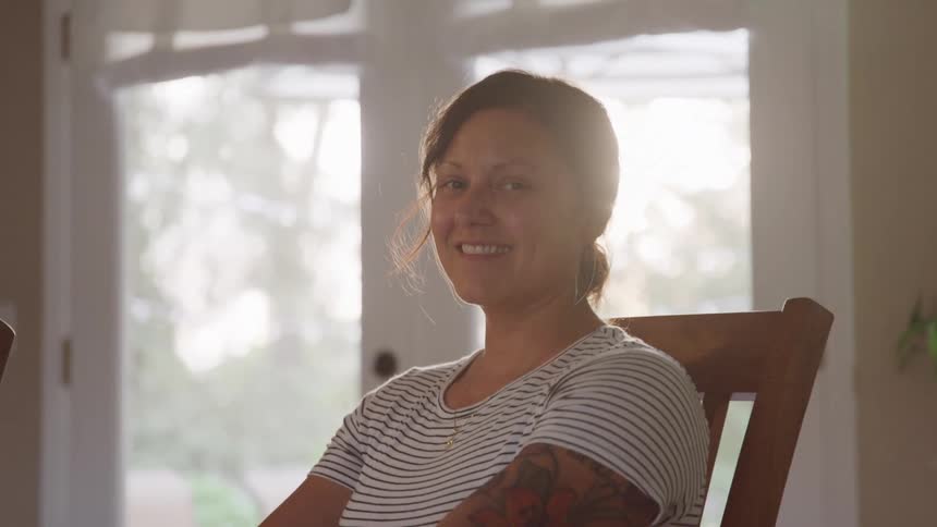 Woman sitting on a chair smiles softly in a sunlit room