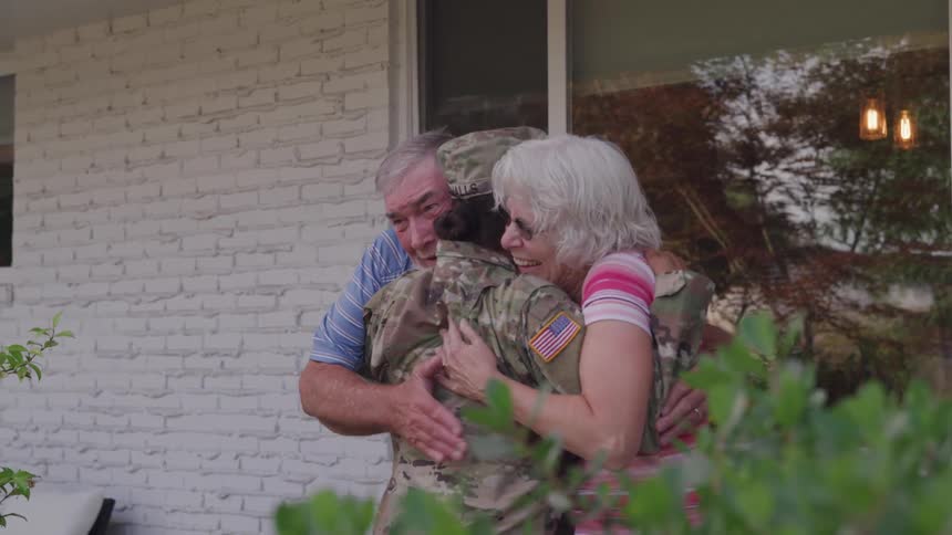 Elderly father and mother embrace their daughter outside their home during daytime on her return from the military