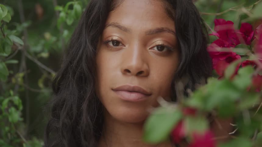 Woman with a calm expression looking at the camera amidst red flowers and green foliage