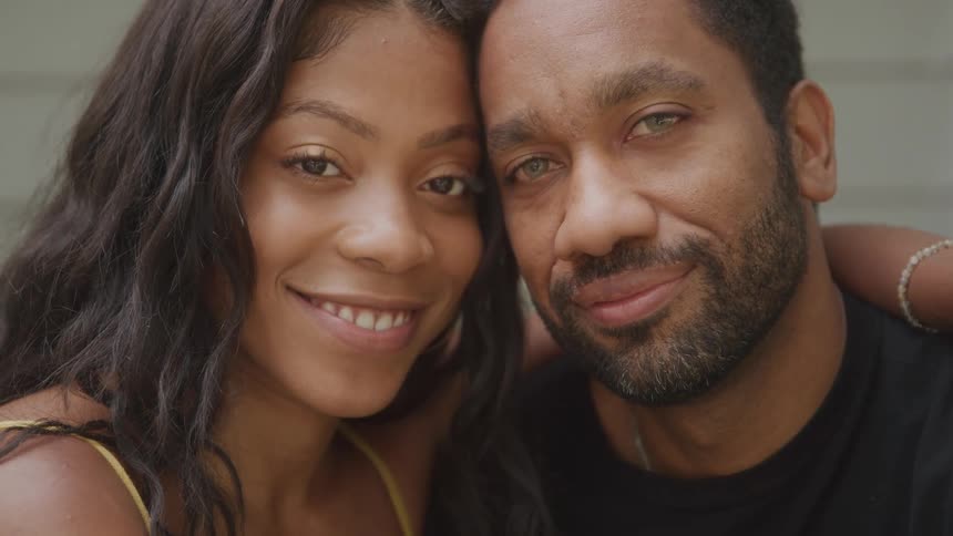 Two people look at each other before leaning their heads together while side hugging