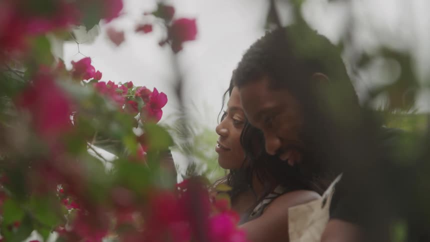 A young man stands beside a woman as they both look at a flower plant in the garden at midday