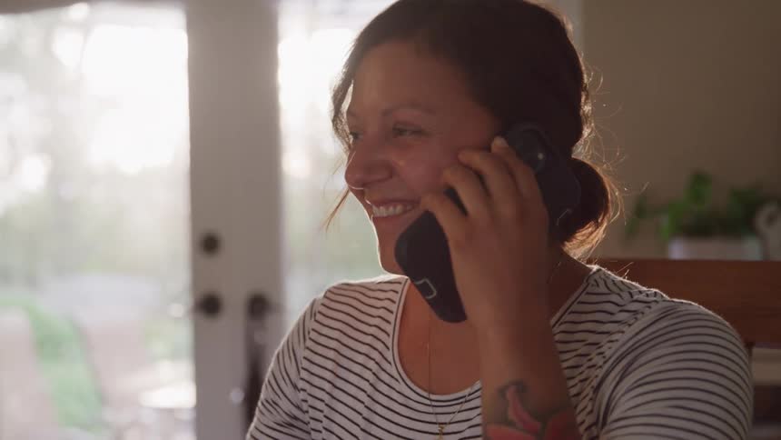 Woman smiles while talking on the phone near a sunlit door
