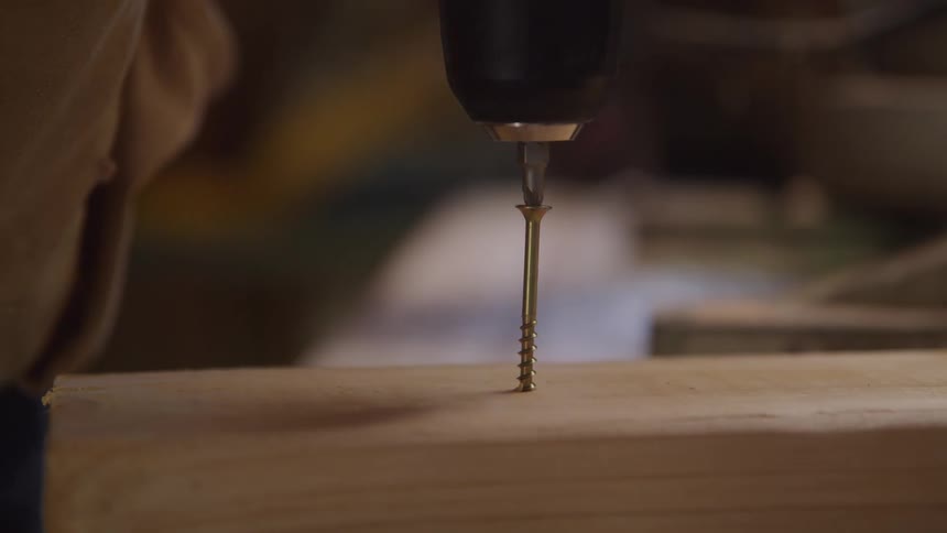 Carpenter drives a screw into a piece of wood using an electric drill fitted with a screwdriver head
