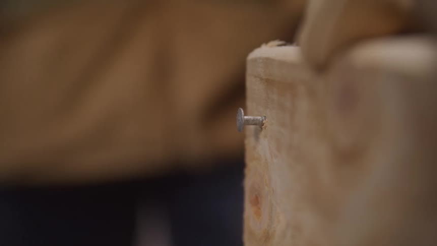 A hammer hits a nail into a piece of wood