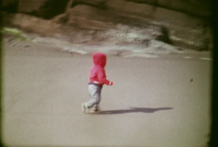 A child in a pink jacket walks down the beach