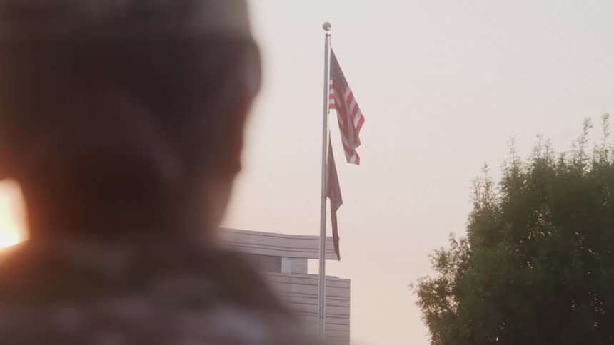 Soldier looks at an american flag raised in front of a building