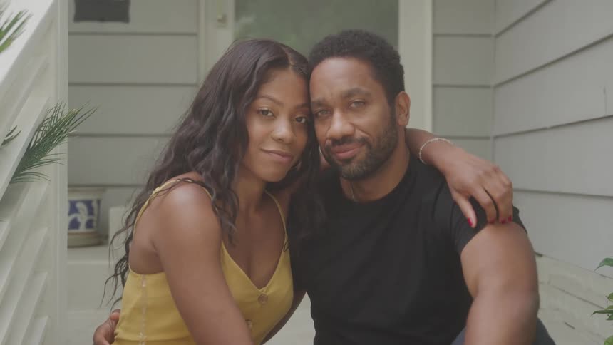 Portrait of a young black couple sitting outdoors at the entrance of a home during daytime