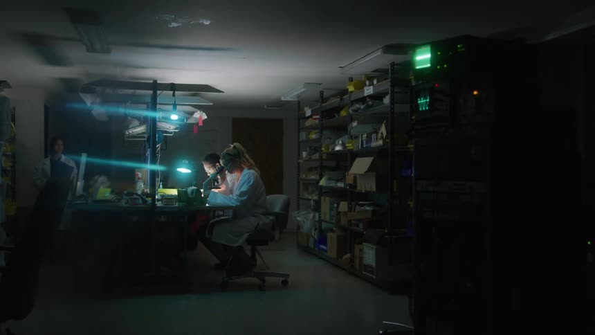 Three lab assistantsone man and two womenwork in a laboratory the man and one woman sit side by side examining various samples while the other woman walks in a circle around the lab