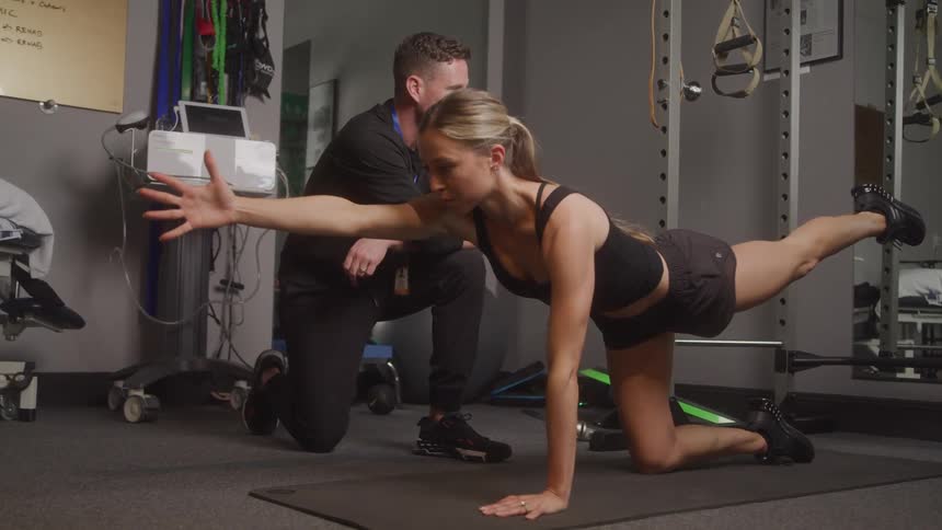 Female client stretching on yoga mat with a male personal trainer at the gyn
