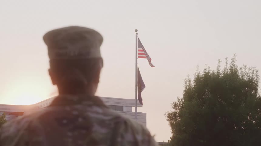 Close up of a female military personnel standing outdoors at sunset in front of an american flag