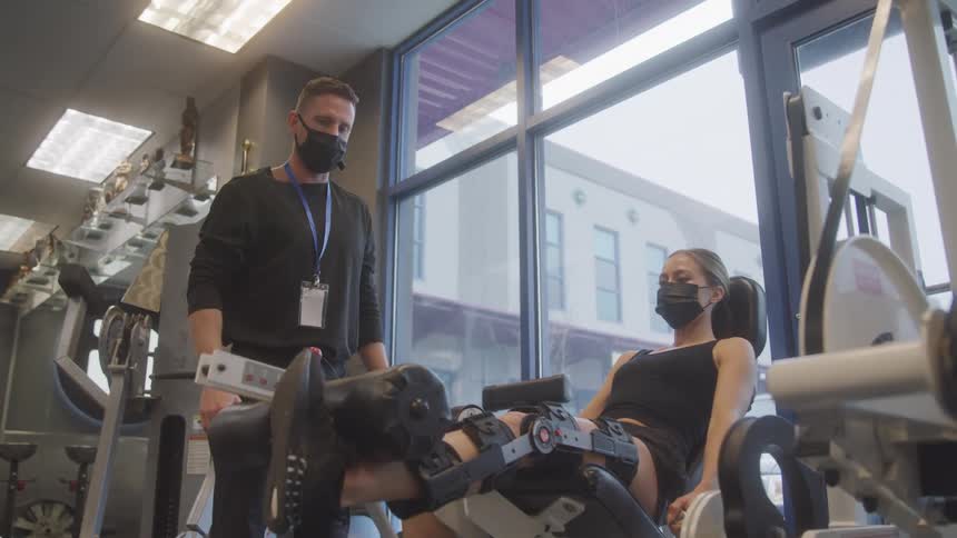Male trainer observes his client using a leg machine while in the gym
