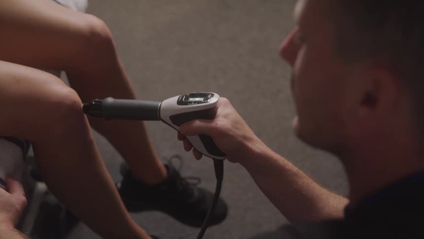 A physical therapist holds a handheld electric therapy device to a patients knee